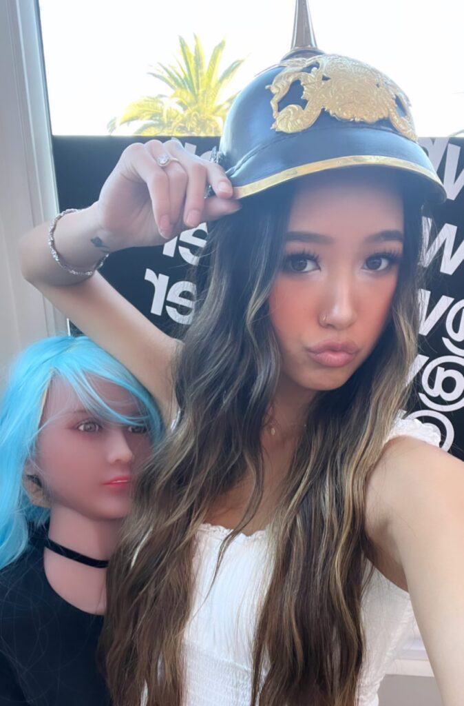 Madysen Vue with long brown hair wearing her German pickelhaube hat is standing next to Whatever Podcast doll with blue hair. Madysen Vue Whatever Podcast Hat Girl Whatever Podcast Guest